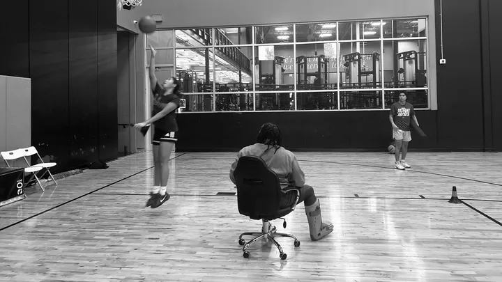 coach with a leg brace sitting in a desk chair on a basketball court