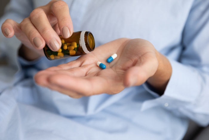 Sick woman hold two pills on hand pouring capsules from medication bottle take medicine.